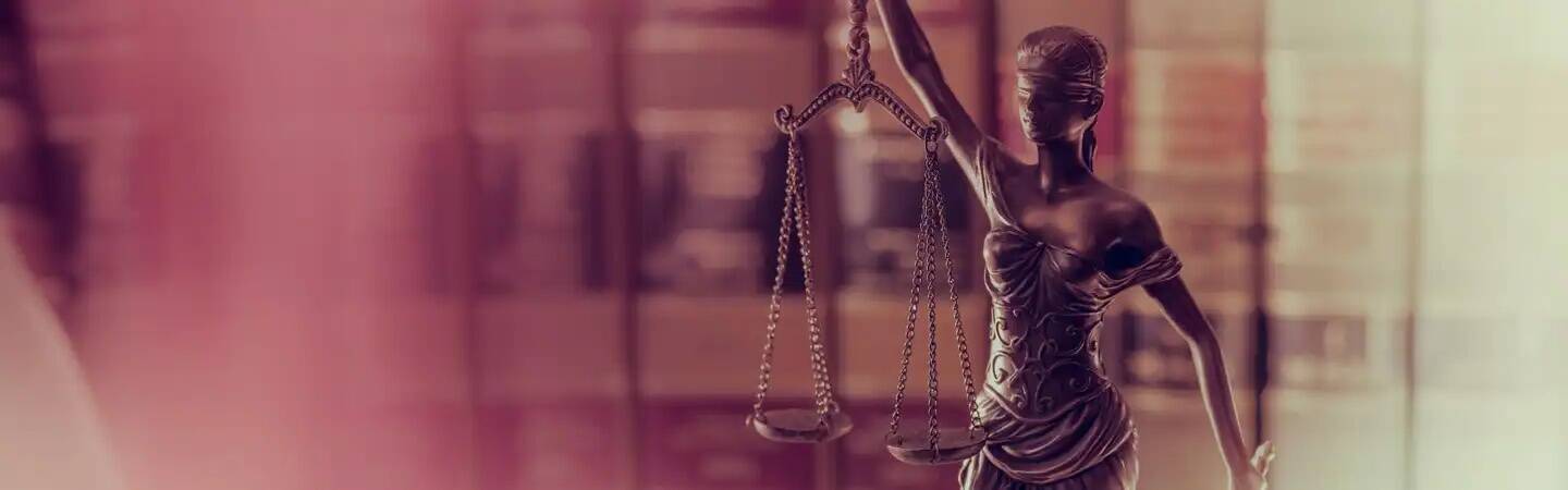Statue of Lady Justice holding scales, with bookshelves blurred in the background.