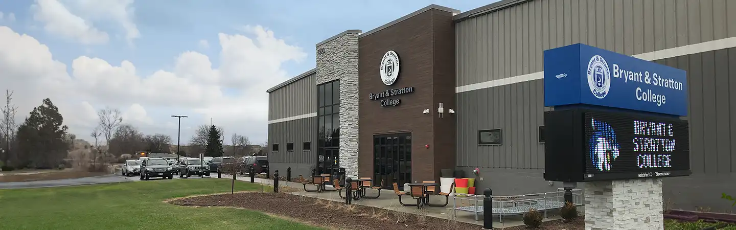 Bryant & Stratton College building with a digital signboard and outdoor seating on a cloudy day.