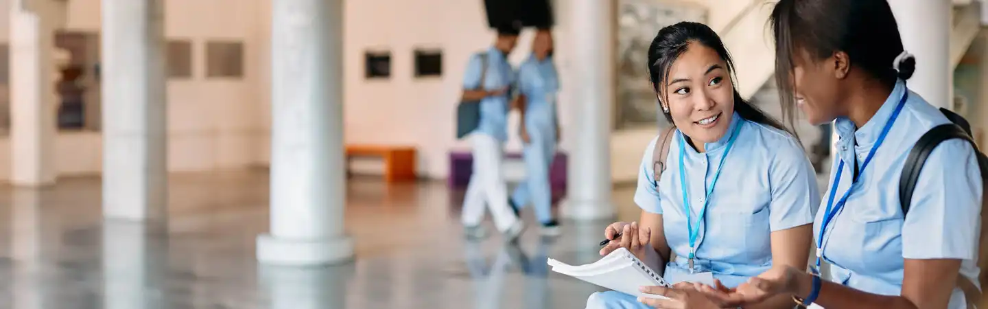 A person in blue scrubs holding a pen and a notebook.