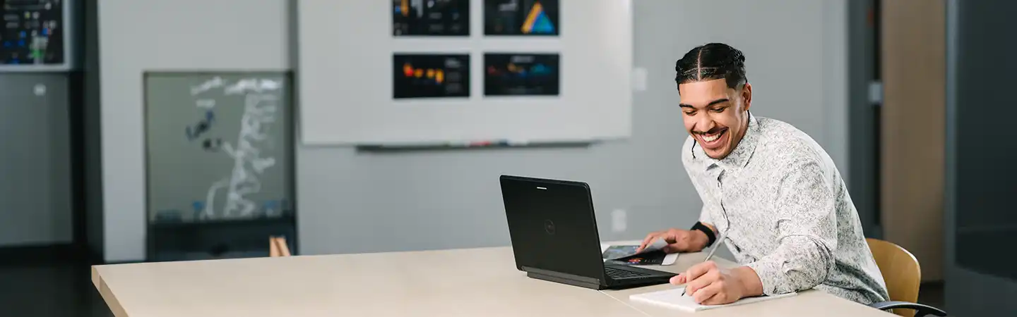Man smiling at laptop while seated in a modern office, with documents and a book on the table.
