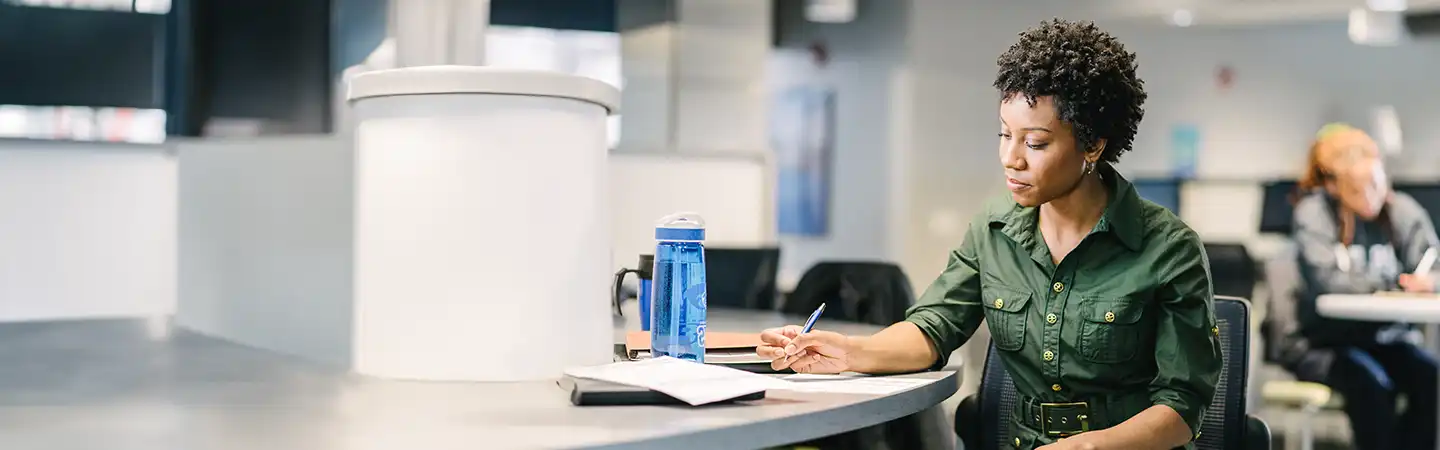 Person at a round table with a blue water bottle, writing on papers, in a bright, modern workspace.