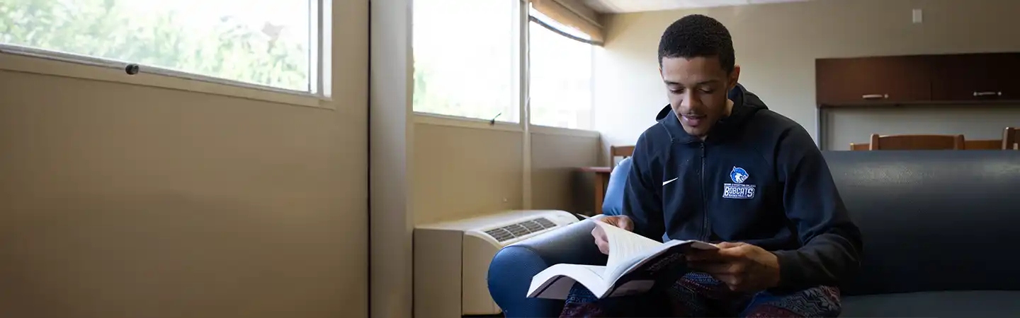 A person sits on a sofa by a window, reading a book in a brightly lit room.